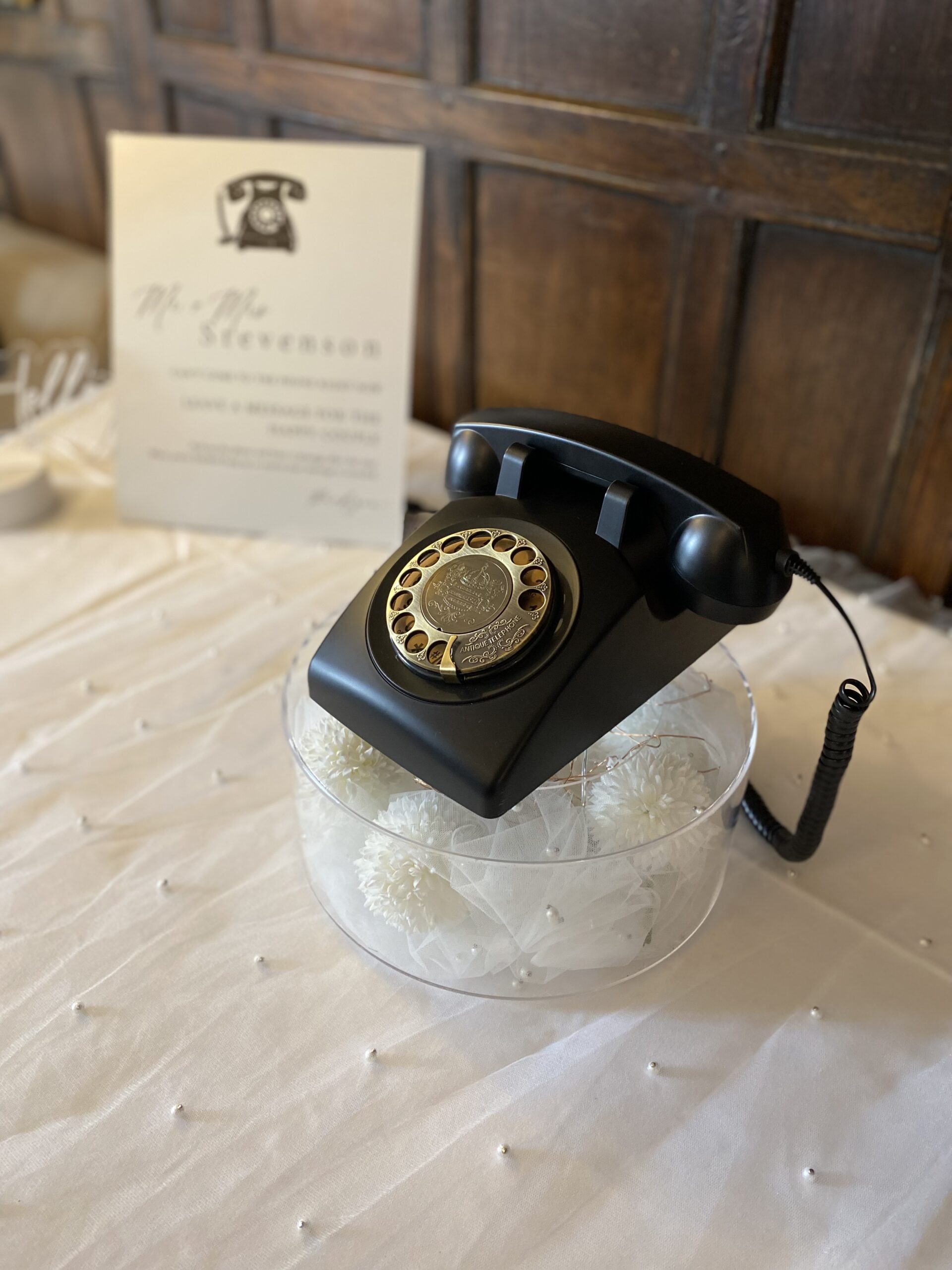 black retro telephone audio guestbook on a white floral wedding stand in front of oak panelled wall