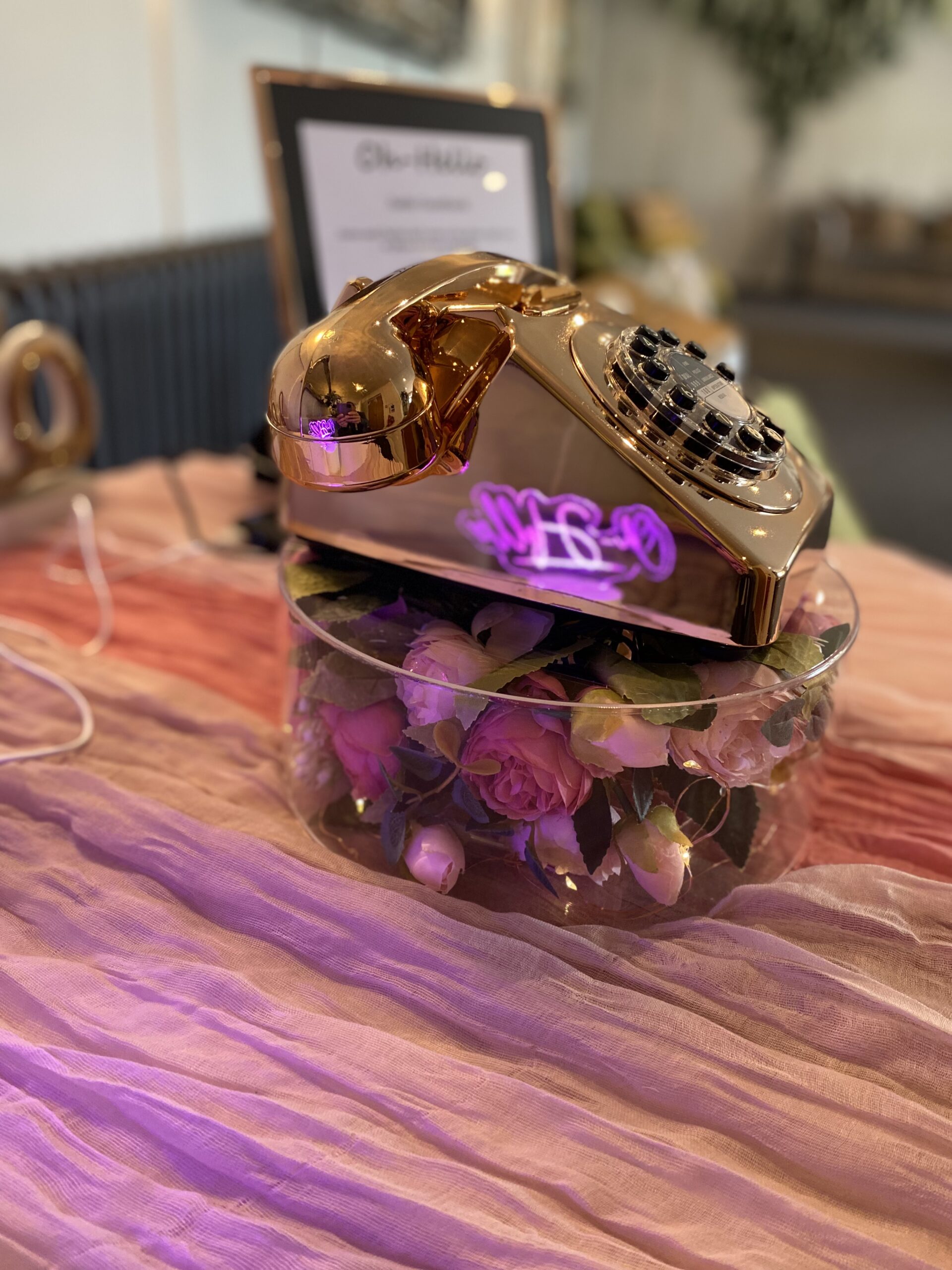 metallic rose gold retro telephone audio guestbook upon a flower filled wedding stand on pink drapes