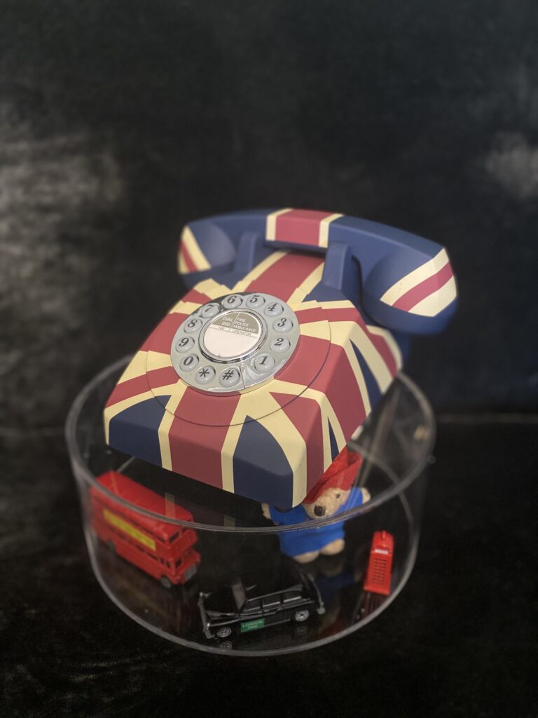 GPO style telephone audio guestbook in British Union Jack colours upon a stand containing a miniature London bus, black cab and Paddington bear all against a black velvet background